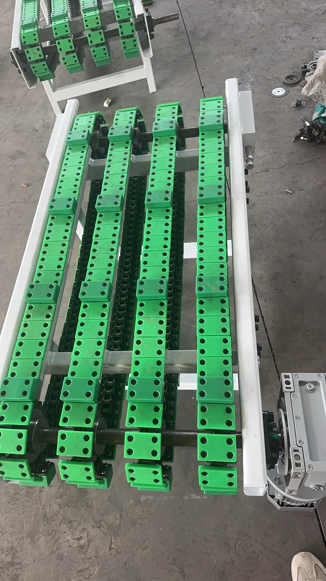 PENKOR chain conveyor — green plastic load carriers mounted on multi-strand roller chains, close-up