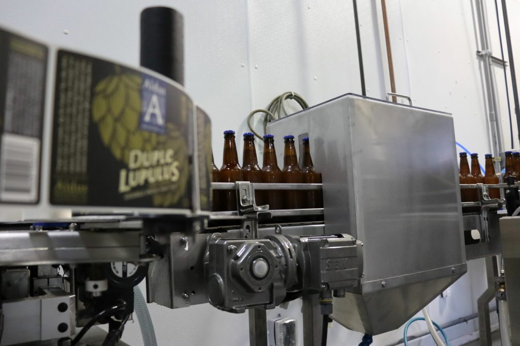 Beverage bottling line — brown glass bottles on a stainless conveyor with an in-line unit (third-party reference photo)