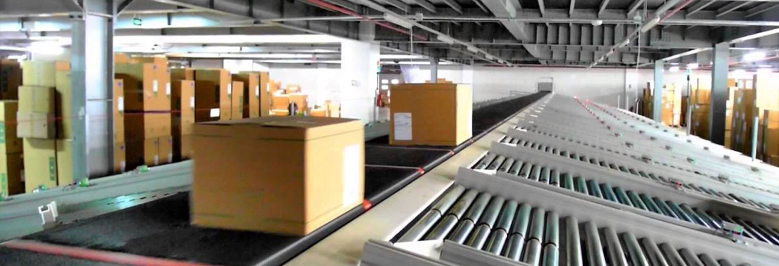 Logistics warehouse — roller/sortation conveyor moving cartons (third-party reference photo)