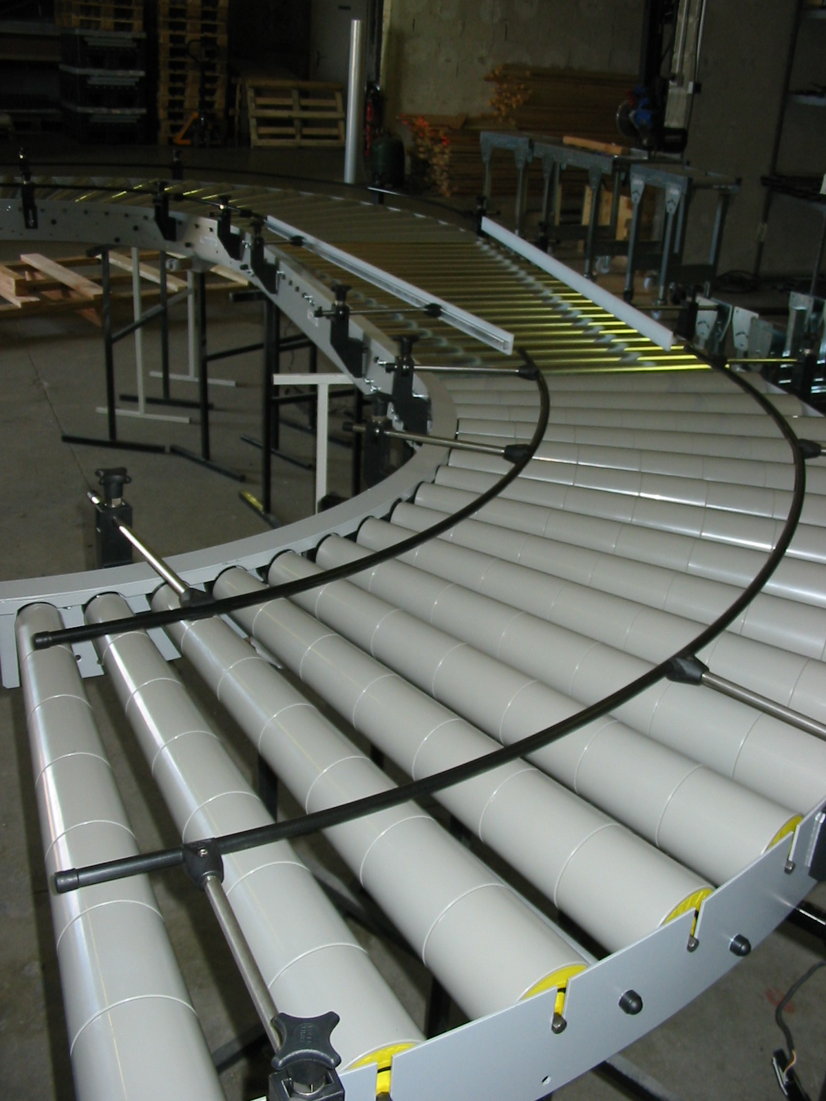Curved (90°) roller conveyor section with curved guide rails in a workshop (third-party reference photo)