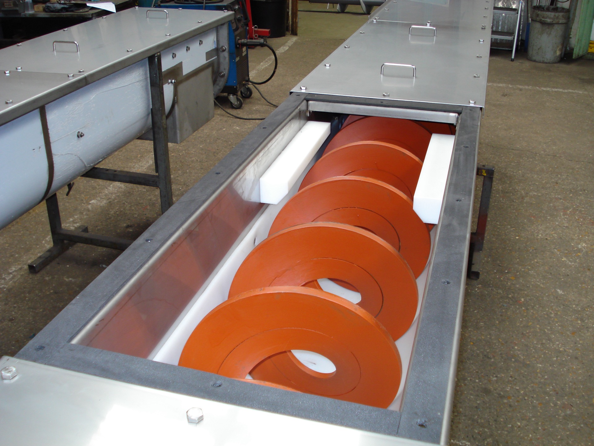 Third-party reference photo — a shaftless (centreless) screw conveyor; the trough cover is open to show the spiral flight and side wear liners (a structure display, not in operation)